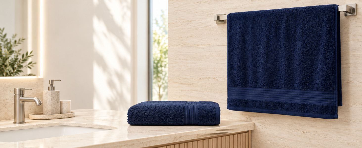 Navy bath towel hanging on a towel bar beside a folded bath towel on a stone vanity.