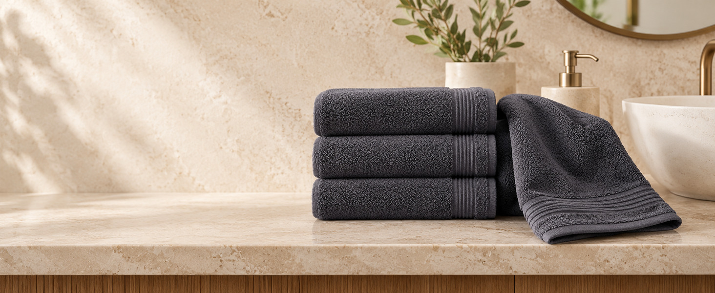 Stack of dark gray hand towels beside a draped hand towel on a stone vanity.